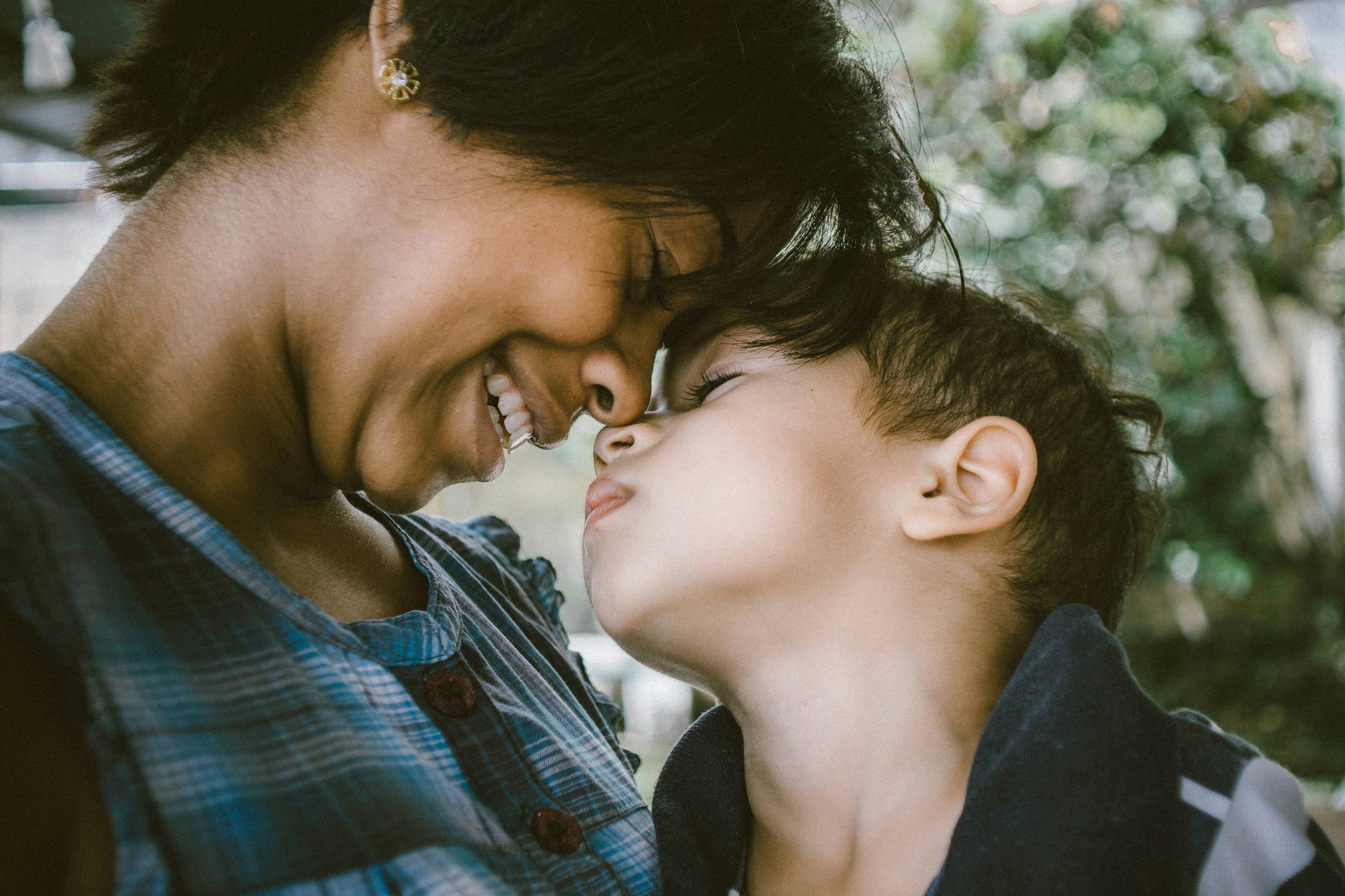 A parent and young child touching foreheads in warm light